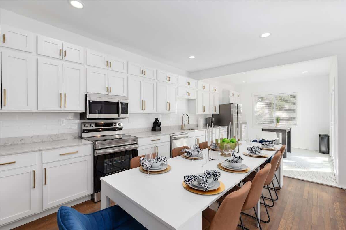 A modern kitchen with white cabinetry, stainless steel appliances, and a dining area set for six.