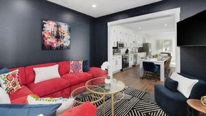 A modern living room with a red sofa, a glass coffee table, and a kitchen visible through an open doorway. - 5BR Detroit near Downtown • 3 King Beds Sleeps 14 (Detroit)
