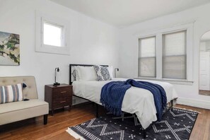 A bedroom with a bed, a nightstand, a dresser, a window, and a painting on the wall.