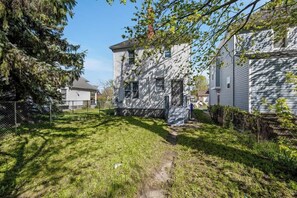 A two-story house with a visible front yard and a fenced backyard. - Spacious Home • 6 Beds + Free Parking • 5 min DT (Detroit)