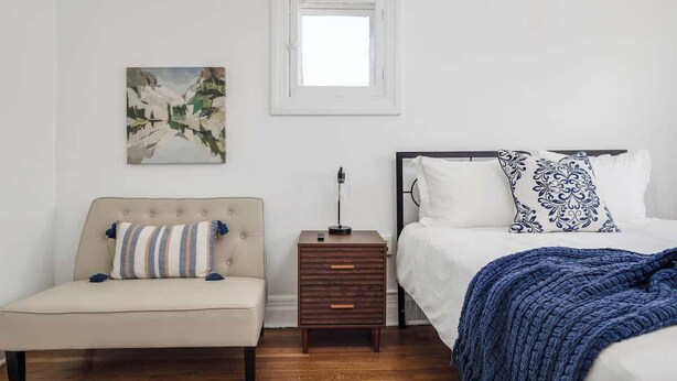 Un dormitorio con cama, mesita de noche, lámpara y un cuadro en la pared.