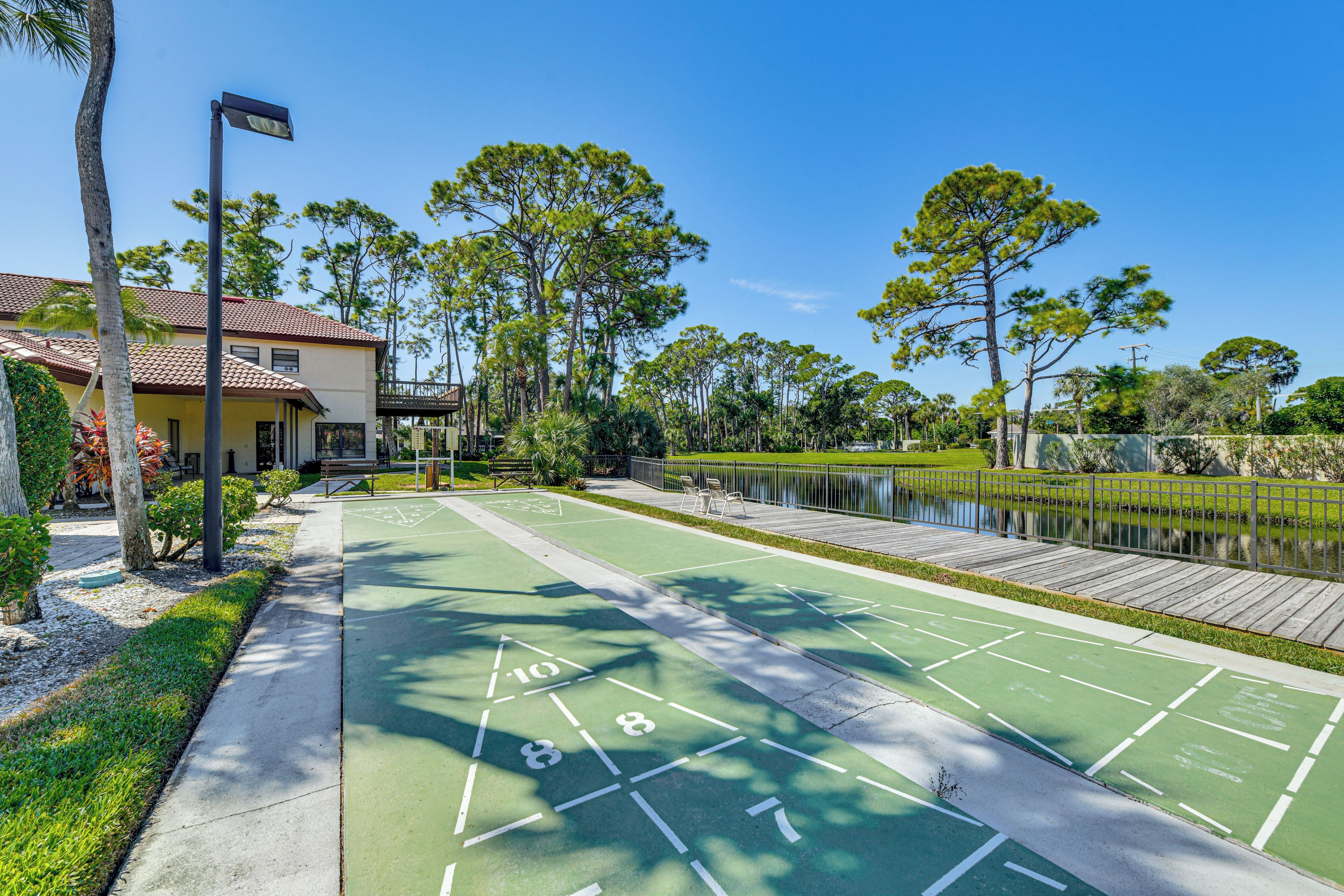 A green outdoor shuffleboard court adjacent to a building with a tiled roof.