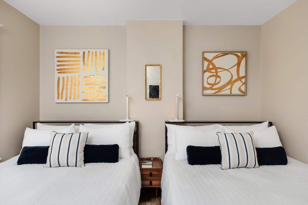 A hotel room with two beds, a mirror, and abstract wall art.