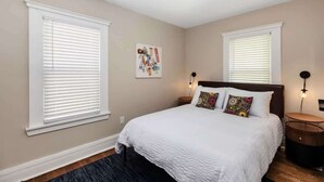 A bedroom with a large bed, two bedside tables, a wall-mounted artwork, and a ceiling light. - Stylish & Comfortable 6BR • Sleeps 16 • Parking (Detroit)
