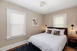 A bedroom with a large bed, two bedside tables, a wall-mounted artwork, and a ceiling light. - Stylish & Comfortable 6BR • Sleeps 16 • Parking (Detroit)