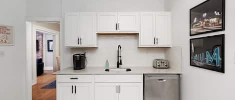 Una cocina moderna con armarios blancos, un lavavajillas de acero inoxidable y una cafetera negra.