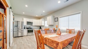 Una cocina moderna con gabinetes blancos, electrodomésticos de acero inoxidable y un comedor con una mesa dispuesta para cuatro.