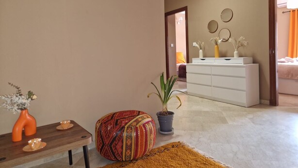 A modern living room with a wooden table, a colorful pouf, a potted plant, and a white dresser with decorative items. - Cosy apartment in the heart of the medina (Marrakech)