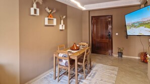 A dining area with a wooden table and chairs, a television mounted on the wall, and a door leading to another room. - Cosy apartment in the heart of the medina (Marrakech)