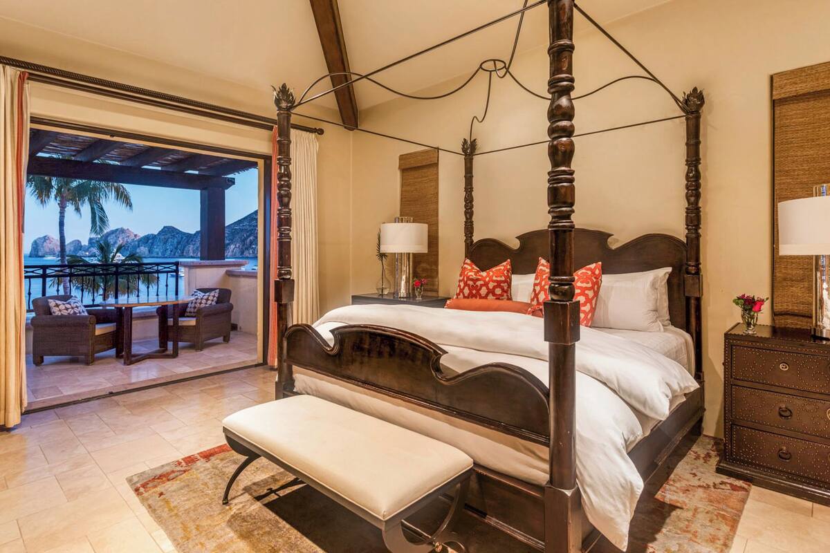 A four-poster bed with a bench, a nightstand, and a view of the ocean.