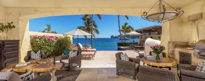 An outdoor patio with wicker furniture, a round wooden table, and a grill. - Hacienda Beach Club & Residences (Cabo San Lucas)
