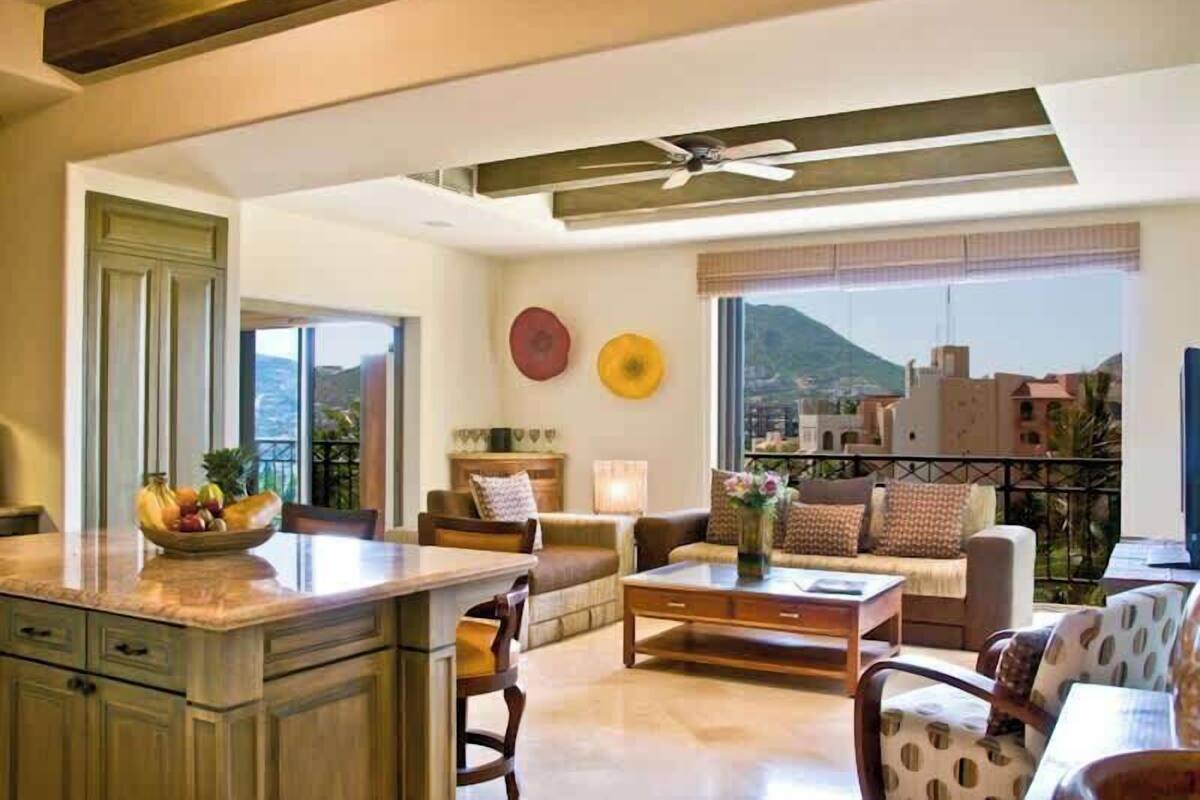 A spacious living room with a large window, a ceiling fan, and a view of the cityscape.