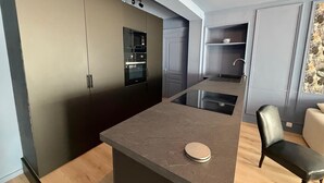 A modern kitchen with built-in appliances, a central island, and a seating area with a chair. - Grand Théâtre view - Stylish 60m2 apartment (Bordeaux)