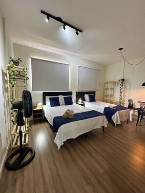 A hotel room with two beds, a standing fan, a table, and a chair. - AP Smart Hub Agro (Piracicaba)