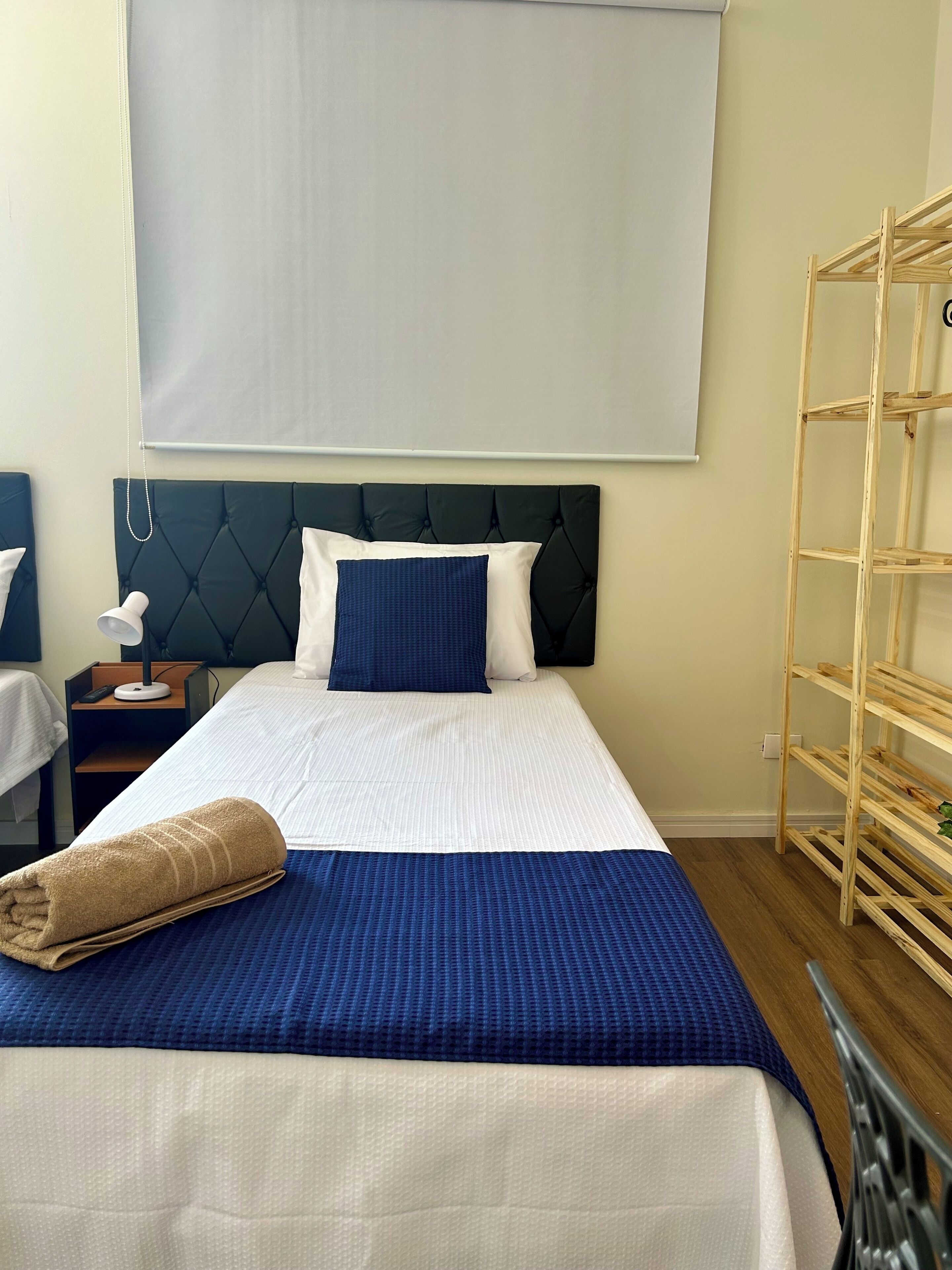 A neatly made bed with a blue and white bedspread, a dark headboard, and a wooden ladder shelf to the right.