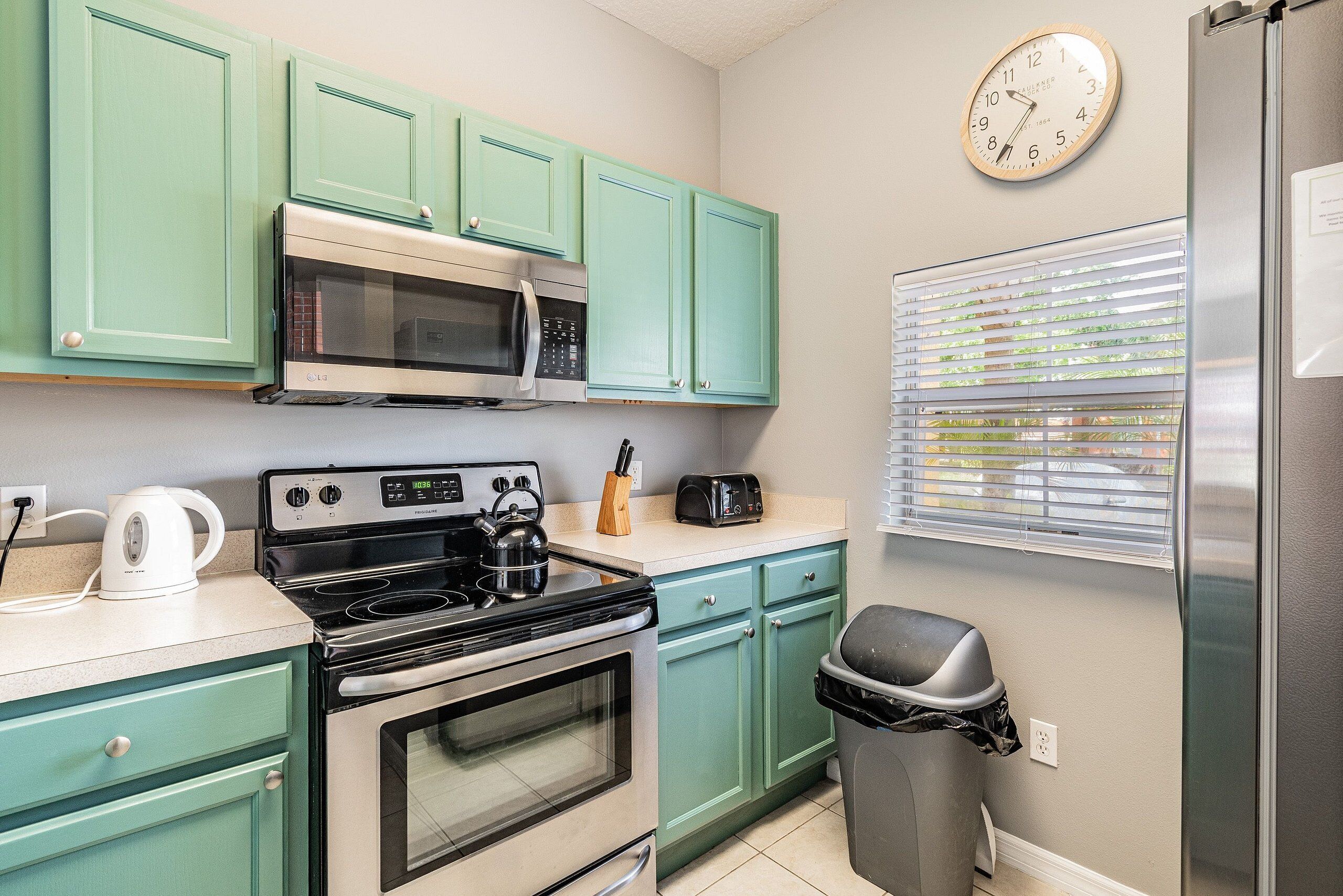 A kitchen with teal cabinets, a microwave, a stove, and a trash bin.