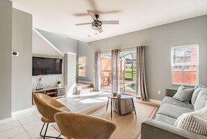 A modern living room with a flat-screen TV, a ceiling fan, a sofa, and a dining area with a table and chairs. - Encantada Resort Home w/ Priv Pool Near Disney (Kissimmee)