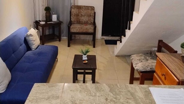 A living room with a blue sofa, a patterned armchair, a small table with a plant, and a staircase with a black railing. - Bungalow Turrent, 5 minutes from Playa Mocambo, Boca del Rio Veracruz (Veracruz)