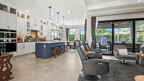 Een moderne keuken met witte kastjes, een centraal eiland en barstoelen. Er is een eethoek met een groot raam en uitzicht op de omgeving.