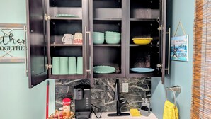 A kitchen with a dark wooden cabinet containing various dishes and a coffee maker. - Tranquil studio with AC in quiet Merritt Island neighborhood (Merritt Island)