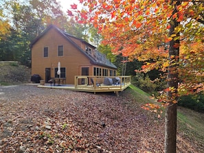 A log cabin with a deck, outdoor seating, and a covered grill area.