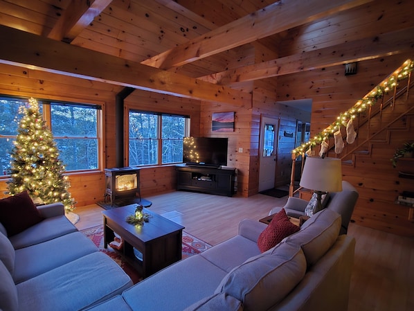 A cozy cabin interior with a fireplace, a television, a sofa, and a Christmas tree.