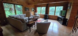 L’intérieur chaleureux d’un chalet avec un canapé, un fauteuil, une table, une lampe et une cheminée.