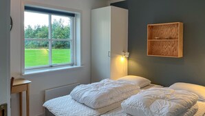 Ein Schlafzimmer mit einem Bett, einem Fenster mit Blick auf eine grüne Wiese, einem an der Wand befestigten Regal und einem Nachttisch.