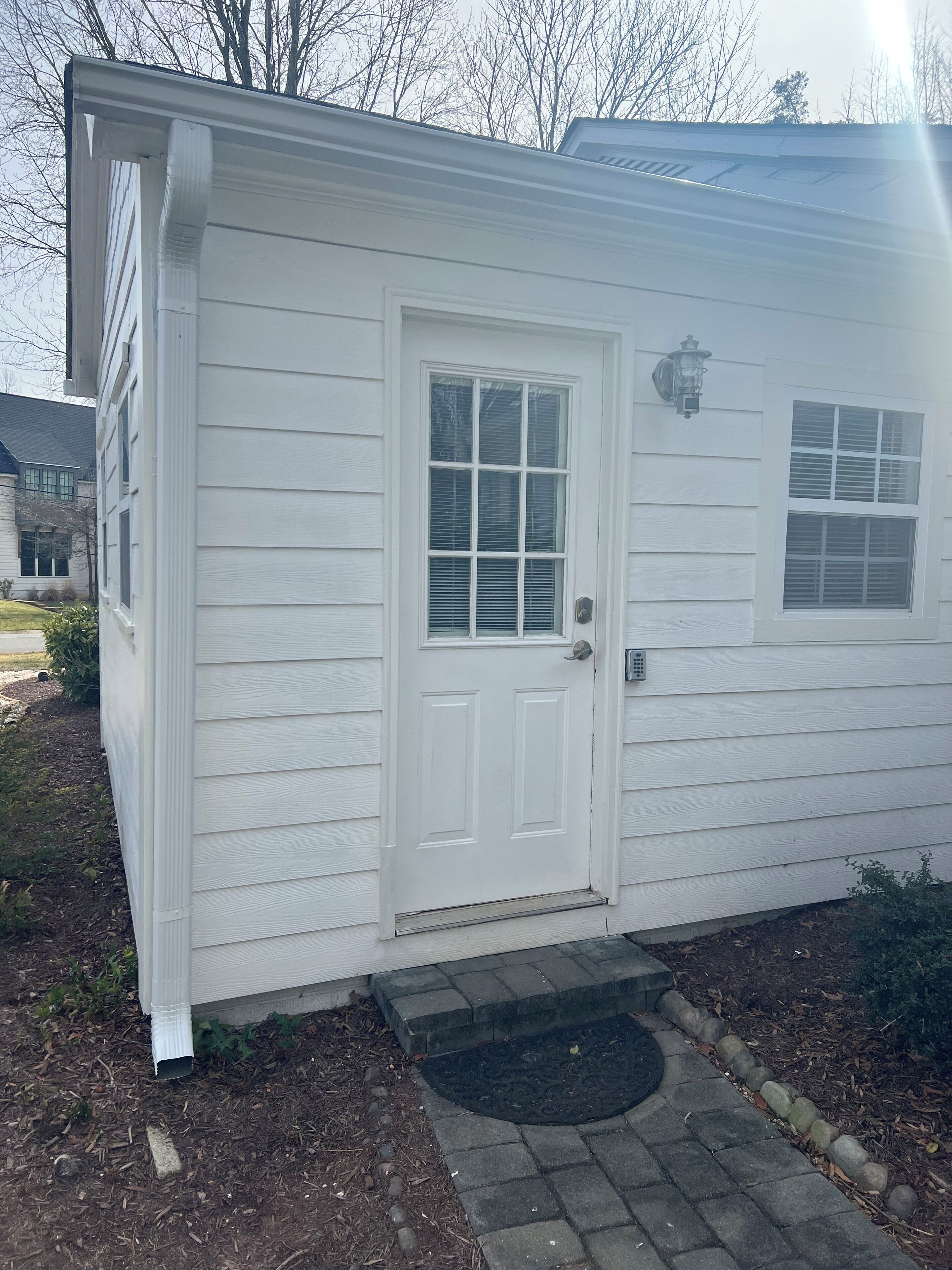 A small, single-story building with a white exterior, a front door, and a small window with shutters.