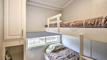 Un lit superposé avec une fenêtre au-dessus, une armoire blanche et une petite étagère avec des livres.