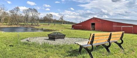 A grassy area with a bench, a pond, and a red barn.
