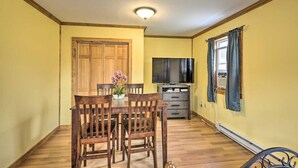 A dining area with a wooden table and chairs, a television, and a window with curtains. - The Cottages and Suite · Poconos Escape (Pleasant Mount)
