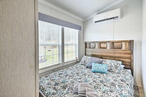 A bedroom with a bed, a window with blinds, an air conditioning unit, and a patterned bedspread.