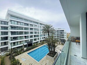A modern hotel with a pool, multiple balconies, and a view of the surrounding area.