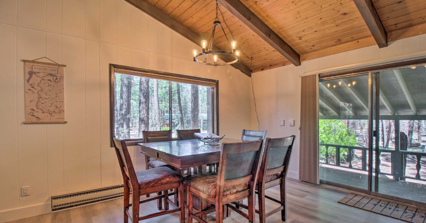 A dining area with a wooden table and chairs, large windows with a forest view, and a hanging light fixture.