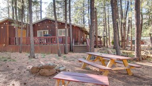 A rustic cabin with a deck and picnic tables in a forested area.