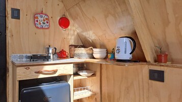 A compact kitchen with wooden walls, a small refrigerator, a kettle, and a toaster.