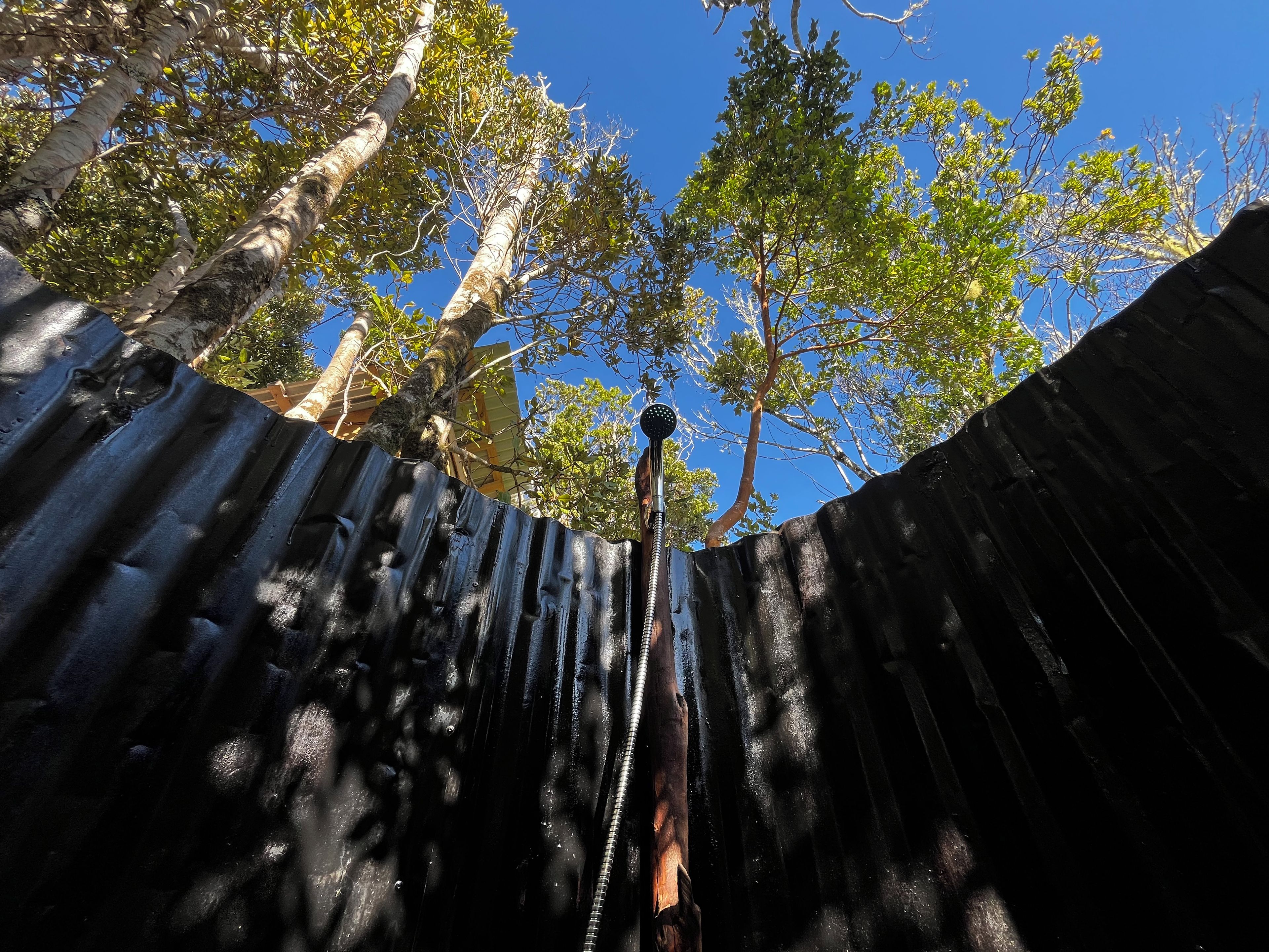 Un mur en métal ondulé, avec un tuyau métallique qui s’étend vers le haut, entouré d’arbres et sous un ciel bleu dégagé.