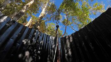 Un mur en métal ondulé, avec un tuyau métallique qui s’étend vers le haut, entouré d’arbres et sous un ciel bleu dégagé.