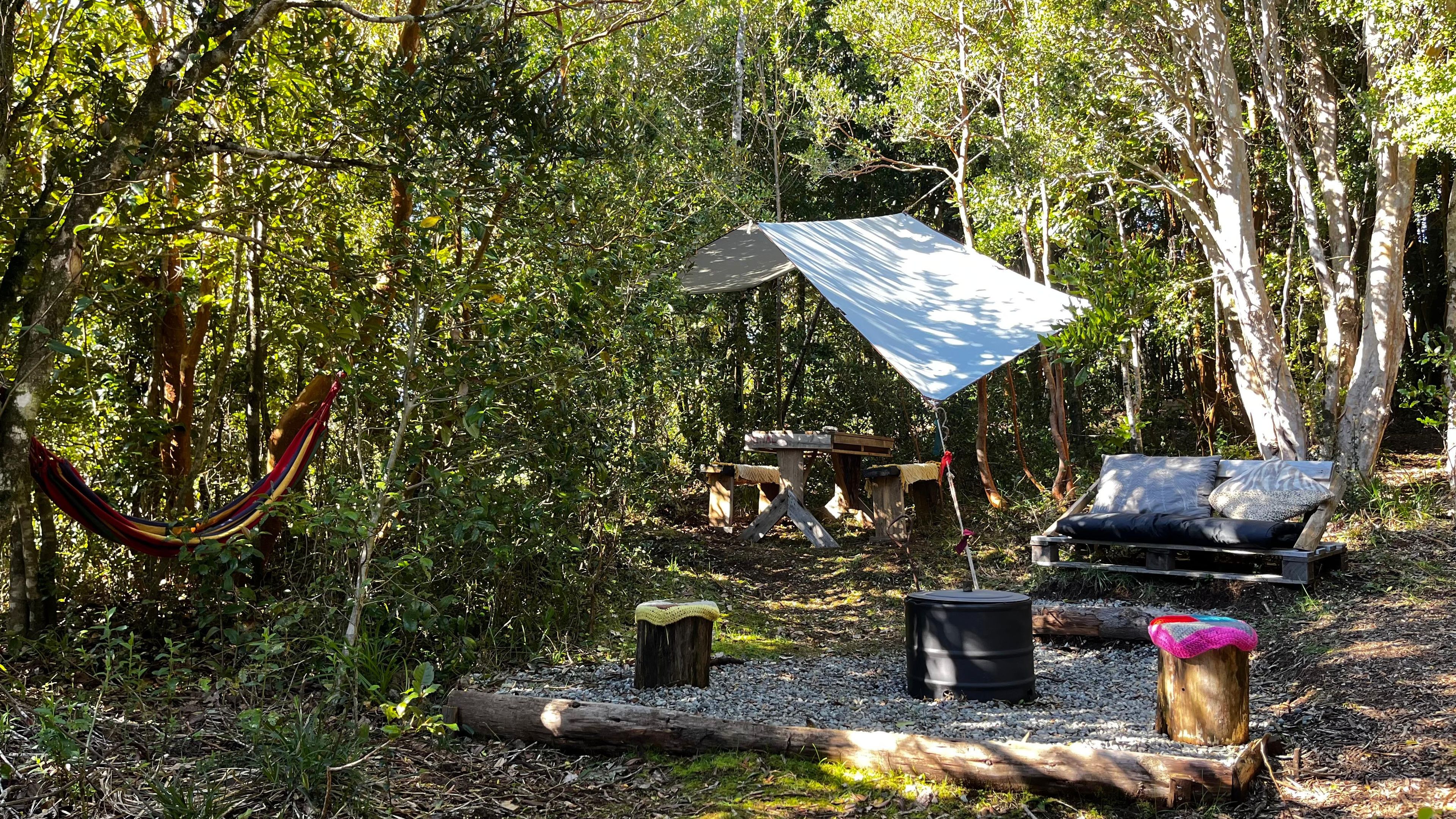 A campsite with a hammock, a wooden bench, a table, and a canopy shelter.