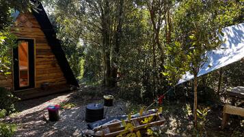 A wooden cabin with a sloped roof, surrounded by dense foliage.