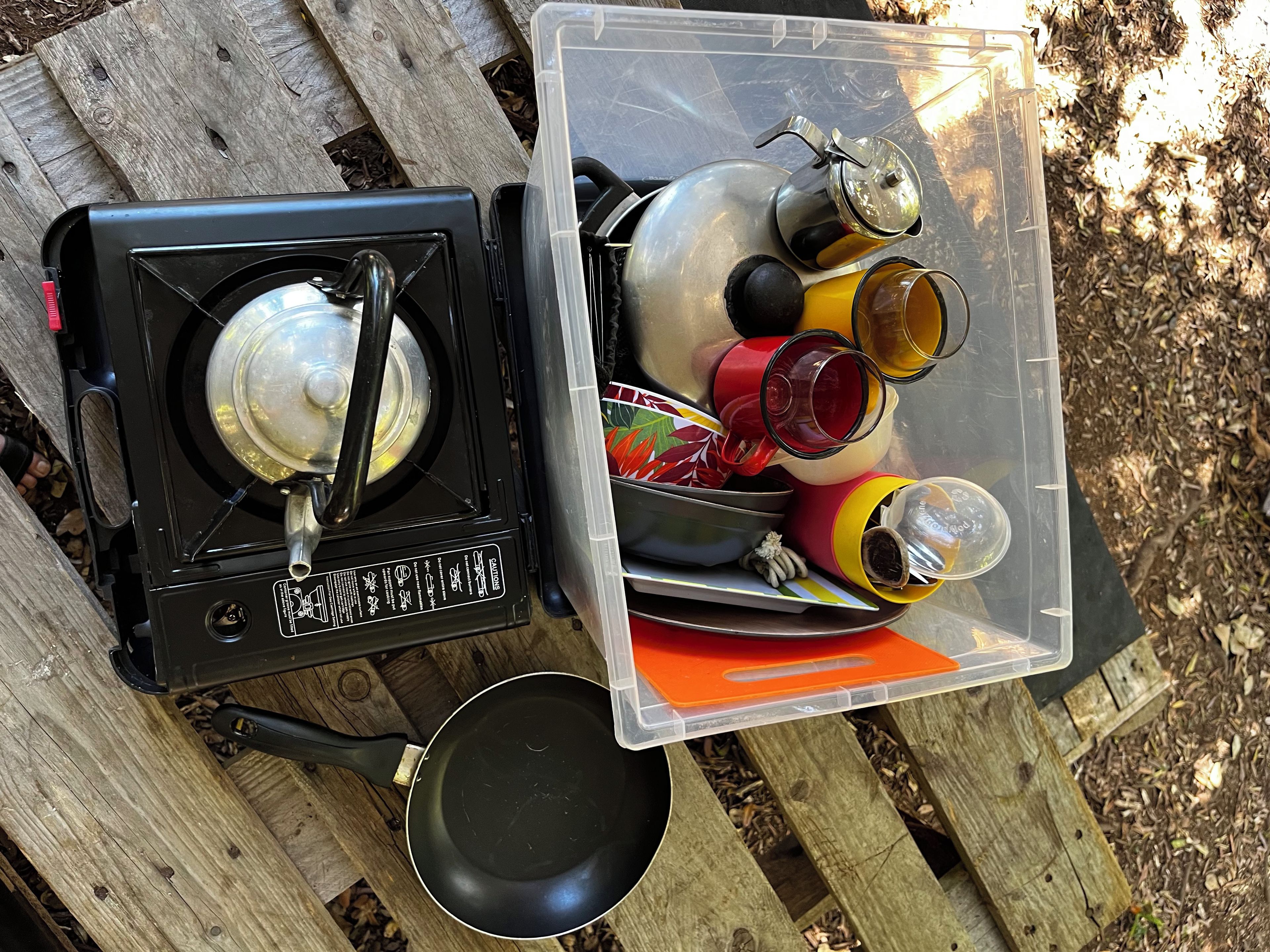 A portable camping stove with a pot and a plastic container holding various items.