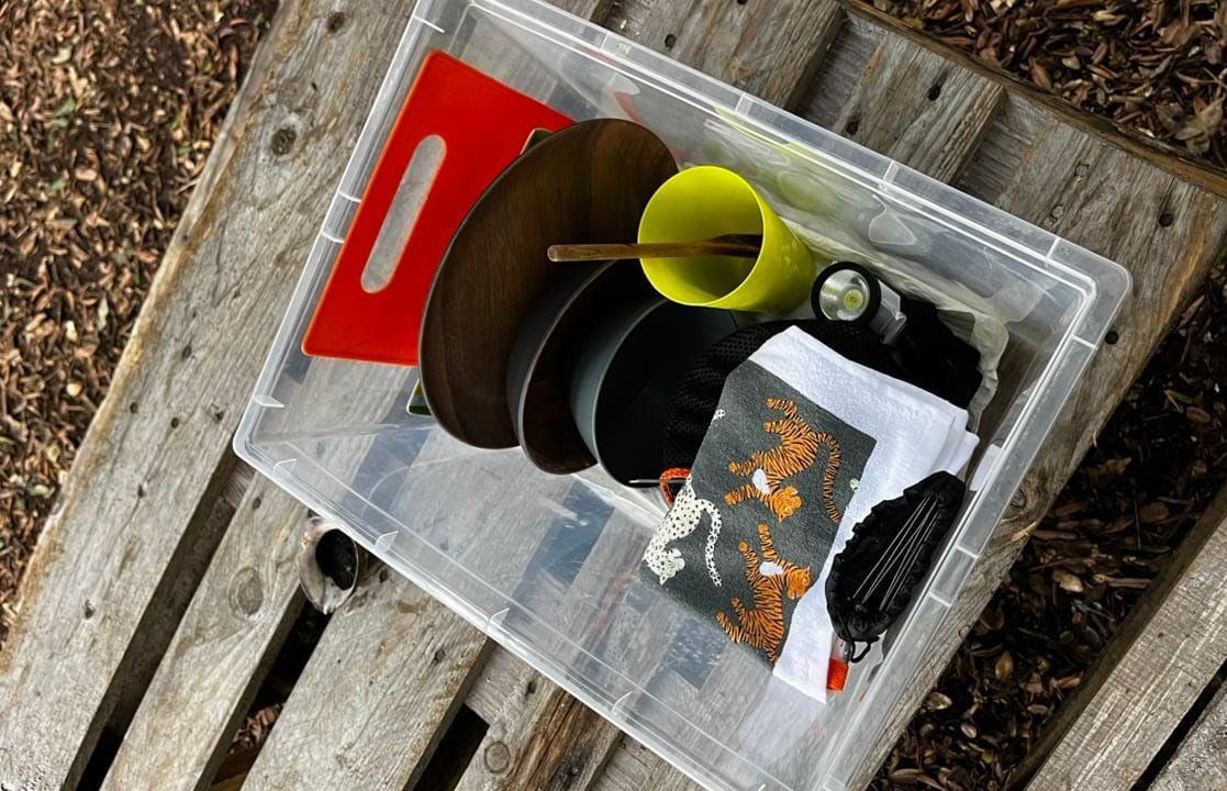 Une boîte de rangement transparente en plastique contenant divers objets, notamment un objet rouge, un gobelet vert et un morceau de tissu à motifs.