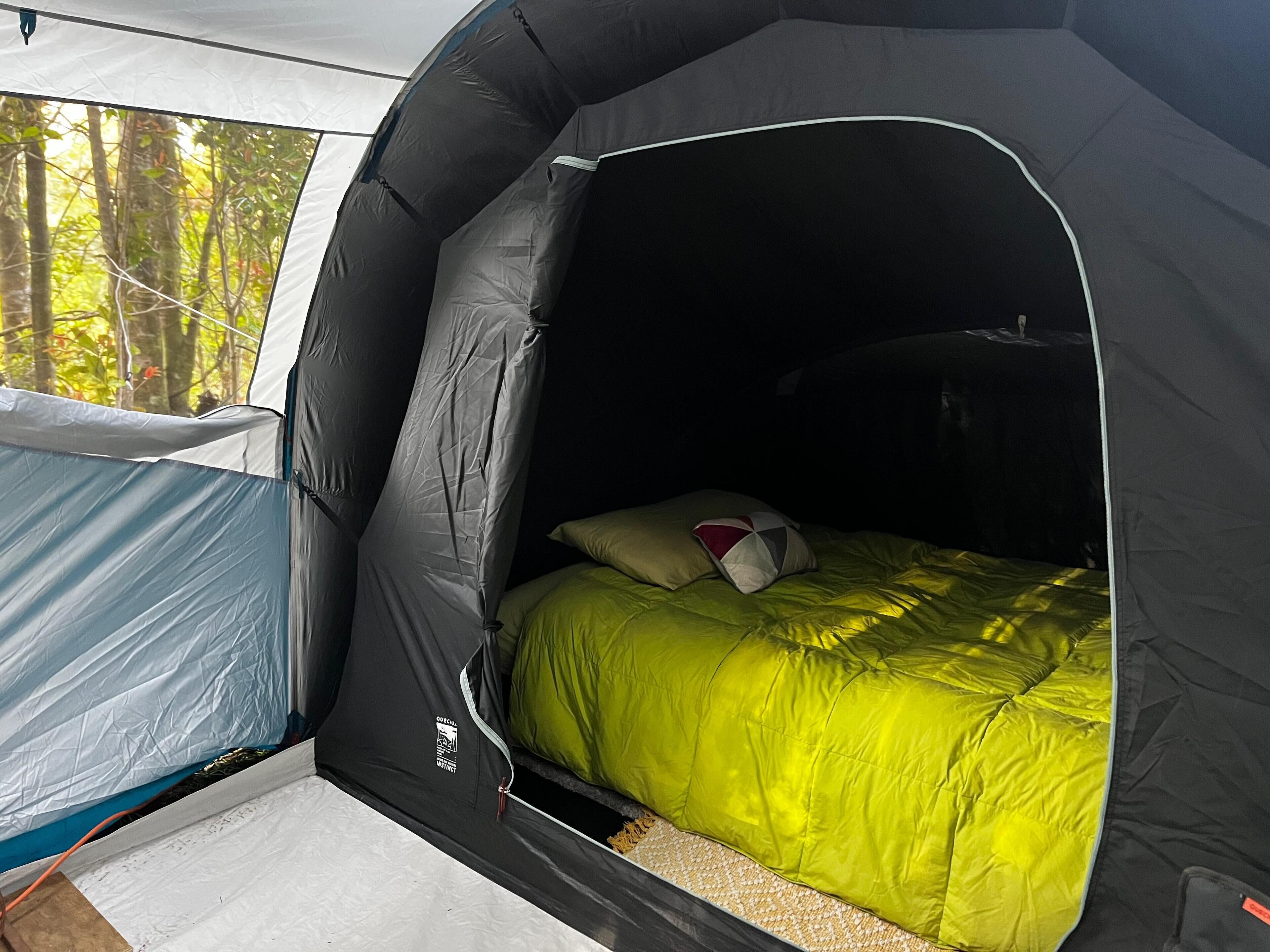 A tent with a bed inside, featuring a green blanket and pillows.