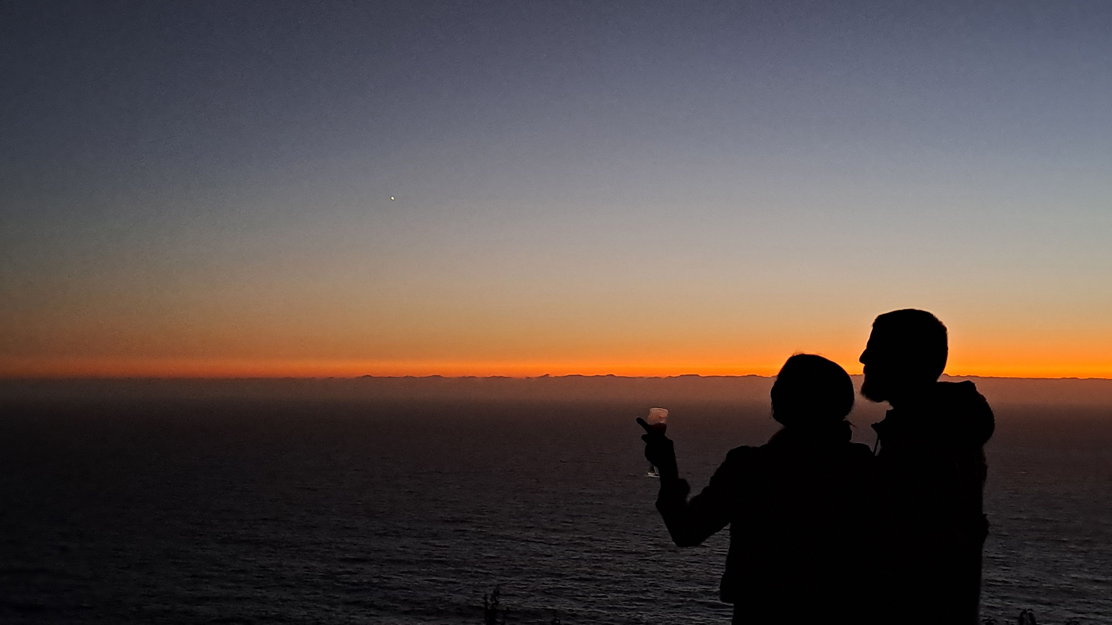 A silhouette of two people against a sunset over a body of water.