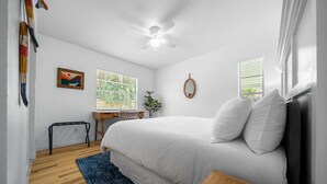 A bedroom with a bed, a desk, a chair, a window, and a ceiling fan.
