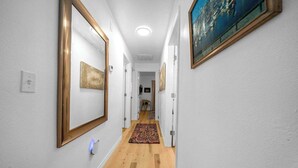 A hallway with white walls, wooden flooring, and a patterned rug.