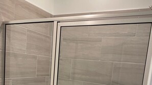 A glass-enclosed shower with a tiled wall and a white bathtub. - 4BR Knightdale Home • Fast Wi-Fi • Near Downtown Raleigh (Knightdale)