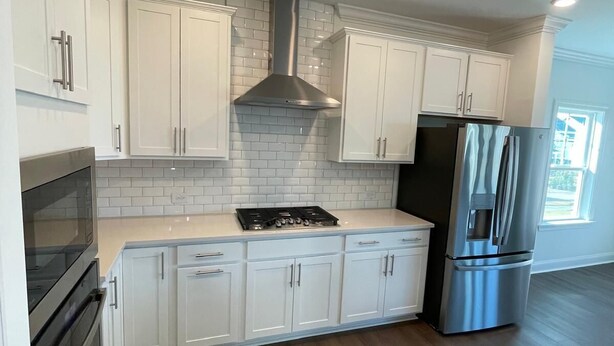 A modern kitchen with white cabinets, a stainless steel range hood, a built-in oven, and a stainless steel refrigerator. - 4BR Knightdale Home • Fast Wi-Fi • Near Downtown Raleigh (Knightdale)