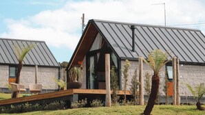 Um edifício moderno com telhado inclinado, deck de madeira e um jardim com cadeiras e plantas.